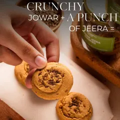 A hand reaches for a Jowar Jeera cookie, showcasing its perfect, crumbly texture. These cookies are my take on a traditional favourite, made with wholesome jowar flour and a punch of jeera for that perfect chai-time snack.