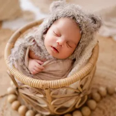 I love capturing newborns in their sleepy, peaceful state. This little one is nestled in a soft basket, wearing an adorable fuzzy bear hat from my studio's collection.