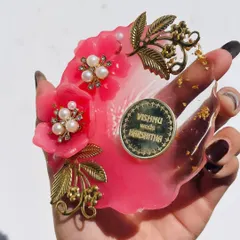 This is a close up of one of my Milni coin plates. I design these decorative resin plates especially for the Milni ceremony at weddings. This one is a vibrant pink flower shape, adorned with pearls, gold-leaf charms, and a custom coin with the couple's names.