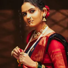 A captivating portrait focusing on the side profile of a model in a Nauvari saree, highlighting the traditional Nath and jhumka earrings against a dark, moody background.