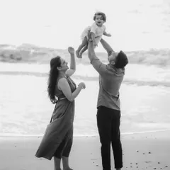 A joyful black and white scene of a father lifting his child up towards the sky on the beach. The composition captures a sense of freedom and fun during a family seaside outing.
