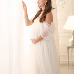 Looking towards the light, this mother-to-be is captured in a moment of quiet anticipation. The bright, airy setting and flowing white gown enhance the dreamy and ethereal quality of the photograph.