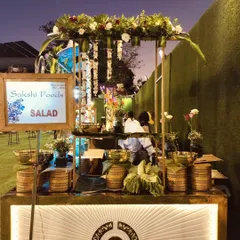 My team setting up a rustic-themed salad bar for an outdoor event, featuring fresh flowers, hanging decorations, and a variety of salad bowls.