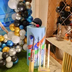 A close-up of a pedestal decorated with cricket equipment props like a bat, ball, and helmet.