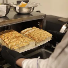 The process of creation begins with the best ingredients. Here, our chef takes freshly baked focaccia bread out of the oven, ready to be served at an exclusive sit-down dinner.