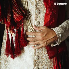 The finest details define our craftsmanship. This close-up highlights the intricate brocade fabric, custom-wound buttons, and the rich texture of a handcrafted groom's sherwani, showcasing the quality that goes into every piece.