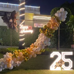 The warm lighting on the palm tree complements the golden tones of the balloon garland in this stylish outdoor anniversary decoration.