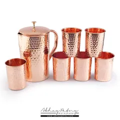 This is a catalogue-style image of a hammered copper jug and glass set. The pure white background ensures that the customer's focus is solely on the product's texture, color, and craftsmanship.