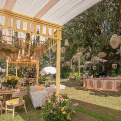 A wide view of the brunch setup, featuring a yellow canopy, a curved bar with rattan details, and dozens of hanging wicker lanterns creating a whimsical overhead installation.