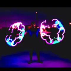 An artist holds two pixel poi, creating intricate, glowing patterns in the dark. This act is a true visual treat.