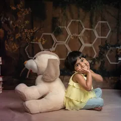 A sweet and shy pose from a toddler during her creative studio photoshoot. Surrounded by stacks of books and her favorite stuffed animal, she shows off her charming personality.