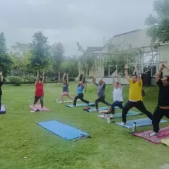 A group of students holding Virabhadrasana I (Warrior I) in the park. Practicing on the grass challenges our balance and grounds our energy.