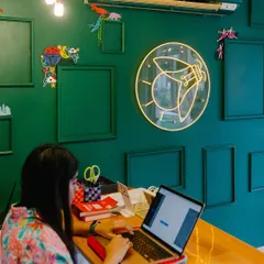 This is my happy place, right at the front desk, surrounded by creativity. The green wall and our firefly neon sign are the heart of the studio, welcoming everyone who comes to make art with us.