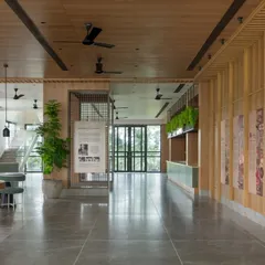 A wider view of the spacious auditorium lobby. This multi-functional pre-event area includes casual seating, a refreshment counter, and informational displays, all designed with a warm and natural material palette.