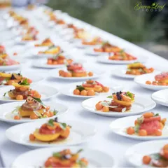 A long table set with dozens of individually plated appetizers, ready for a large event. This style of pre plated service is an elegant alternative to a traditional buffet, ensuring consistency and beautiful presentation.