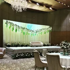 A clean and modern stage for a Roka ceremony at Andaz Delhi. The backdrop of white drapes with a garland of hanging greenery and a neon monogram is both fresh and elegant.