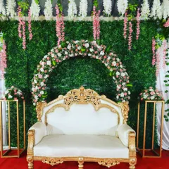 I created this engagement backdrop with a floral arch set against a lush artificial grass wall. The hanging pink and white wisteria flowers add a touch of romance, while the ornate gold and white sofa completes the look.