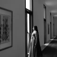 A black and white portrait of the bride, Bandana, looking out a window. The play of light and shadow creates a contemplative and cinematic mood.