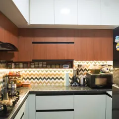 A cozy L-shaped kitchen that pairs wood-finish upper cabinets with light green lower cabinets. The standout feature is the vibrant chevron-patterned backsplash that adds a playful yet sophisticated touch to the space.
