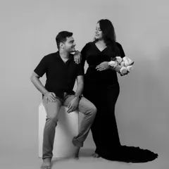 A classic couple's pose in our studio. The mother-to-be holds a bouquet of white roses, adding a touch of elegance to this black and white maternity portrait.