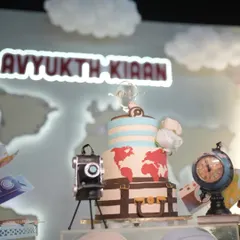 A grand travel-themed dessert station for a first birthday adventure. The setup features a world map backdrop, a suitcase-style cake, and vintage-inspired props like a camera and globe, sparking a sense of wanderlust.