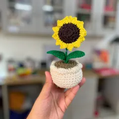 This crochet sunflower in its little pot is held up to show its size and detail. It’s a perfect desk buddy or a cheerful accent for a shelf, bringing a bit of sunshine indoors.