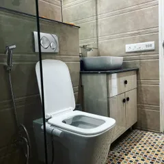 A compact and modern bathroom in Vatika City. The design features a wall-mounted toilet, a floating vanity to save space, and patterned floor tiles that add a decorative touch.