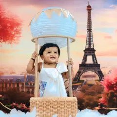 A dreamy Parisian adventure, with a smiling baby in a hot air balloon prop set against a romantic Eiffel Tower backdrop at sunset.