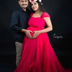 A sweet couple's portrait against a black background. The partner makes a heart shape with his hands on the baby bump, a classic and loving gesture.