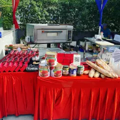 A full view of my catering stall at an outdoor event, featuring a red tablecloth, the portable pizza oven, and a display of ingredients. I create an inviting and professional setup for any function.