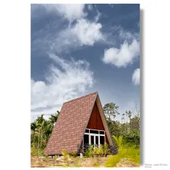 A classic A-frame cabin stands proudly against a bright blue sky in the coffee plantations of Sakleshpur. This image highlights the simple, iconic geometry of the structure and its beautiful rural setting.