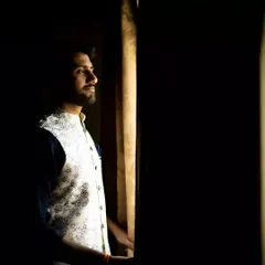A thoughtful portrait of the groom looking out a window. The natural light creates a cinematic mood, capturing a moment of quiet reflection on his wedding day.