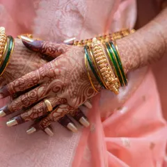 A close-up shot of the bride's hands, adorned with beautiful mehndi and traditional green and gold bangles, during her Haldi ceremony.