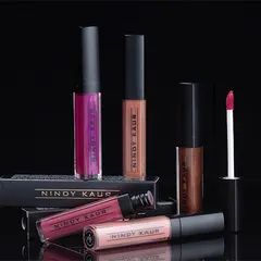 A group shot of various liquid lipsticks against a reflective black background, highlighting the sleek packaging and range of shades for a cosmetic brand's launch.
