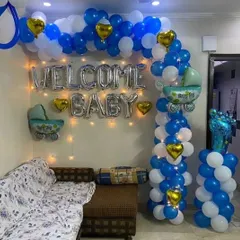 A classic "Welcome Baby" setup for a baby boy. This decoration features a blue and white balloon arch, silver foil letters, fairy lights, and cute baby-themed foil balloons.