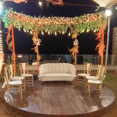 A simple and elegant seating arrangement for a small ceremony or photo spot. The circular stage is topped with a floral arch and hanging lights, creating a beautiful and intimate setting.