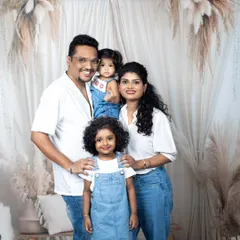 A happy family of four, dressed in coordinated white shirts and denim, sharing a genuine, joyful moment in the studio.