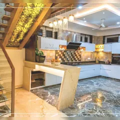 This open kitchen is cleverly integrated under a staircase. It features a breakfast counter, modern appliances, and a mix of marble and tile finishes, proving that any space can be made functional and stylish.