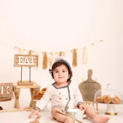 A quiet moment for the little chef. This portrait captures the baby sitting calmly amidst the baking setup, looking directly at the camera with a sweet expression.