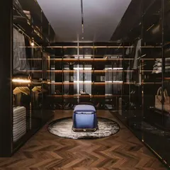 A stunning walk-in closet with dark wood, glass doors, and integrated lighting. This luxurious design provides ample space for clothes, shoes, and accessories, all beautifully displayed.
