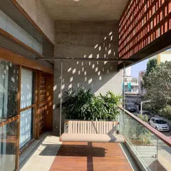 This balcony features a beautiful wooden deck and a hanging swing, with a terracotta jali wall that provides privacy while allowing for airflow and interesting light patterns.