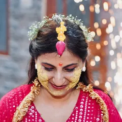 A beautiful, happy moment from a Haldi ceremony. The bride looks down with a smile, her face adorned with haldi and a floral maang tikka, perfectly capturing the spirit of the event.