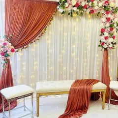I love playing with unique color combinations, like the warm rust drapes paired with soft pink and white flowers in this setup. The asymmetrical floral arch adds a modern touch, while the fairy lights in the background give it a magical glow. This is a great option for a chic and stylish pre-wedding event.