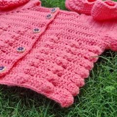 A close-up of the texture on this pink baby sweater. The bobble stitch adds a lovely, playful detail, and the little flower buttons are the perfect finishing touch.