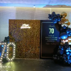A sophisticated black and gold theme for a 70th birthday. This setup includes a gold sequin wall, a personalized sign, marquee numbers, and a stylish balloon garland.