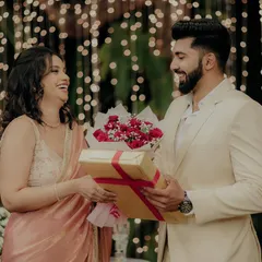 The couple exchanging gifts and flowers in front of a backdrop of beautiful fairy lights, a heartwarming part of their engagement story.