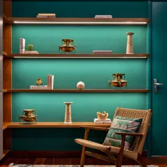 The home office in 'Vasudhalayah' features this stunning curio unit. Washed in emerald green, the floating shelves display the family's cherished heirlooms, turning a functional space into a personal gallery.