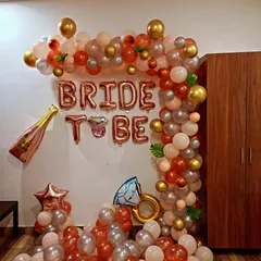 A fun and stylish "Bride to Be" decoration. This home setup features a rose gold and silver balloon arch, foil letters, and champagne and ring-shaped foil balloons.