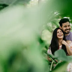 A candid moment of laughter shared between the couple, framed by vibrant green leaves. This style of shooting creates a sense of intimacy, as if we are peeking into a private, happy moment.