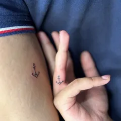 A simple and classic matching tattoo for a couple. A small anchor on the finger and arm symbolizes stability and being grounded in each other.